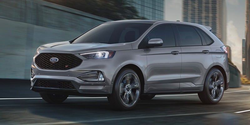 Gray Ford Edge ST SUV moving on a road with blurred city buildings in the background