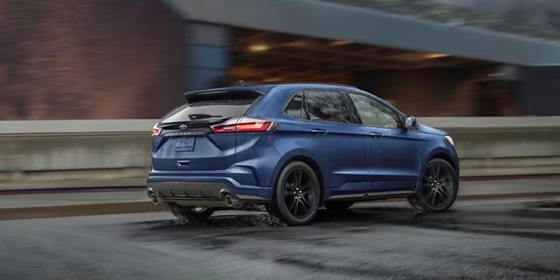 Dark blue Ford Edge SUV driving on a wet road, viewed from the rear three-quarters