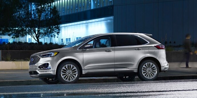 Silver Ford SUV parked on a wet street at night with a building and person in the background