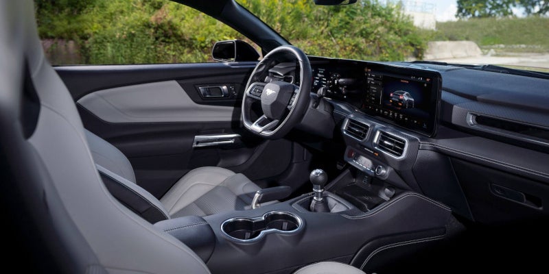 Hands on a Ford Mustang steering wheel with digital dashboard and screen display, driving in a dark tunnel.