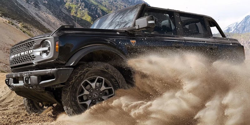 Black Ford Bronco kicking up sand while off-roading in a rocky, mountainous landscape.