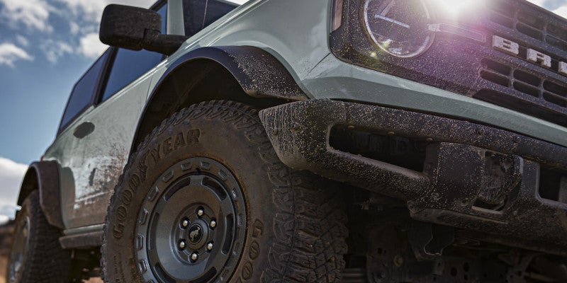 Dusty light-green Ford Bronco, seen from a low angle, highlighting the front tire and bumper.