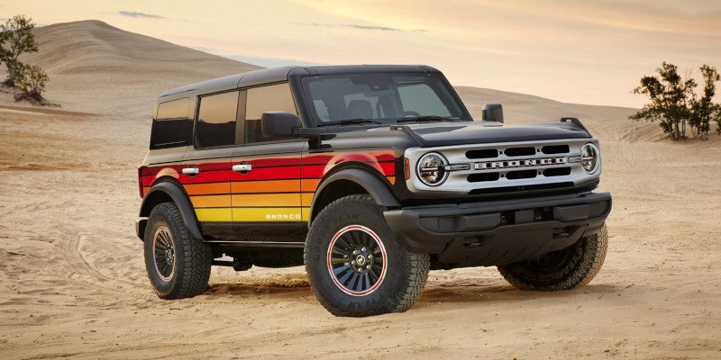 Black Ford Bronco with retro red, orange, and yellow stripes on the side, parked in a sandy desert landscape.