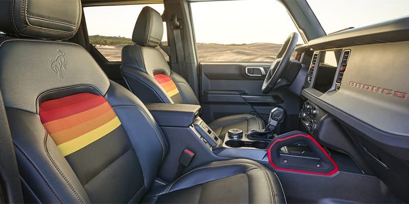 Bronco interior with black seats, colorful red, orange, and yellow striped inserts, and a textured dashboard.