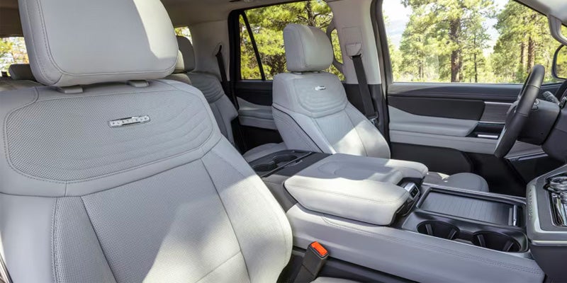 Light gray leather car interior with a view of the front seats, center console, steering wheel, and trees outside.