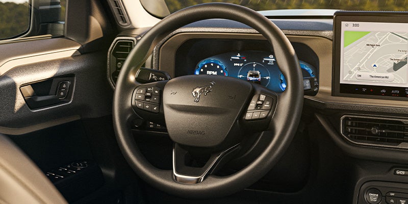 Car interior with a steering wheel showing a Bronco logo, digital dashboard, and an infotainment screen displaying a map.