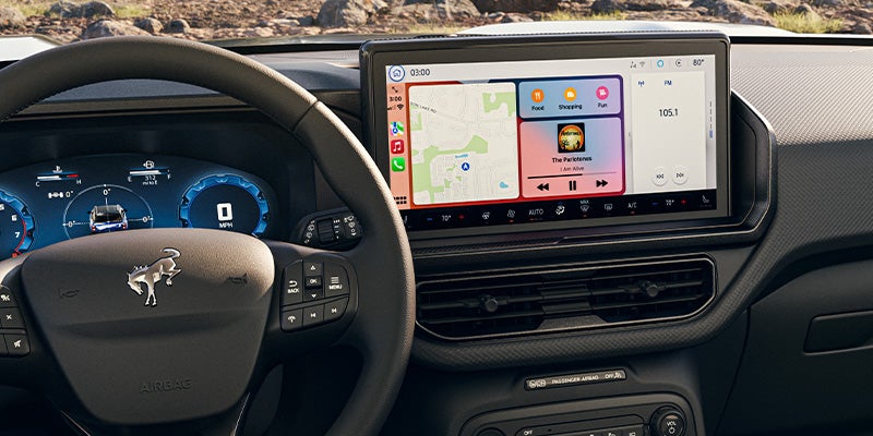 Car interior showing a steering wheel, digital dashboard, and a large infotainment screen with navigation and music apps.
