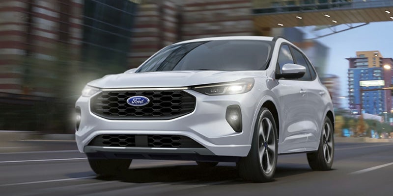 Front view of a white Ford Escape SUV driving in an urban setting with blurred background indicating motion.