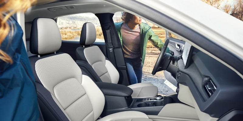 Modern car interior with light and dark two-tone seats. A person in a green jacket stands by the open door.