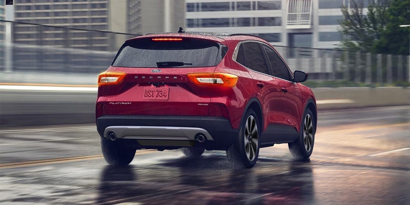 Red Ford Escape SUV driving on a wet road, seen from the rear with a blurred city background.