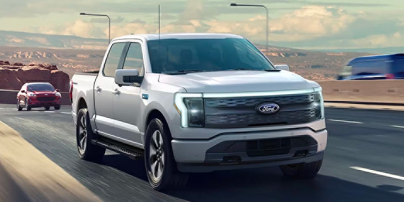 White Ford F-150 Lightning electric pickup truck driving on a highway with a desert landscape.