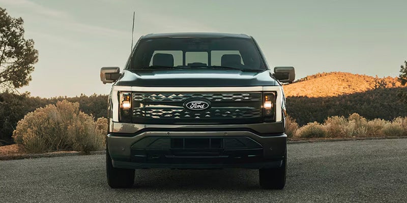 Front view of a dark grey Ford F-150 Lightning electric pickup truck with distinctive LED headlights and grille.