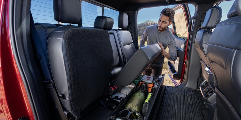 Man lifting a back seat in a red truck to reveal an under-seat storage compartment filled with gear