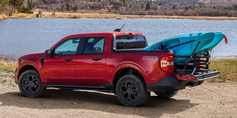 Red pickup truck with a blue kayak loaded in its bed, tailgate down, parked by a lake