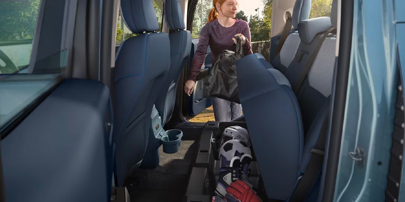 Woman putting a bag into the back of a blue car with rear seats folded
