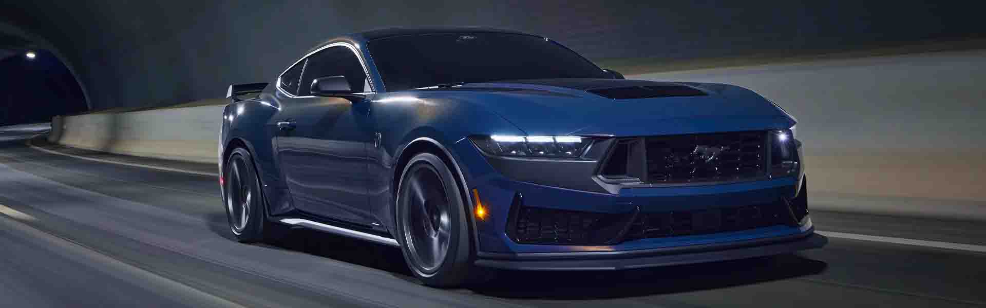 Blue sports car with headlights on driving quickly through a dark tunnel.