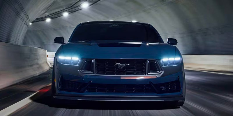 Dark blue Ford Mustang driving head-on through a tunnel with its headlights on.