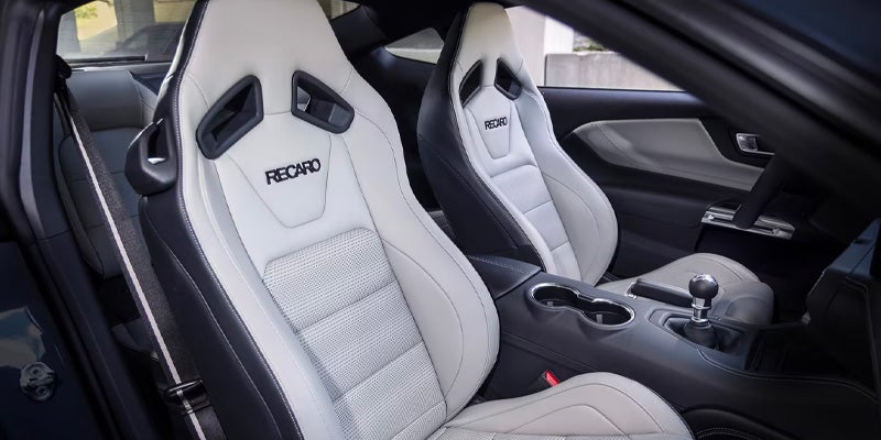 White and black Recaro racing seats and a manual gear shifter in a car interior.