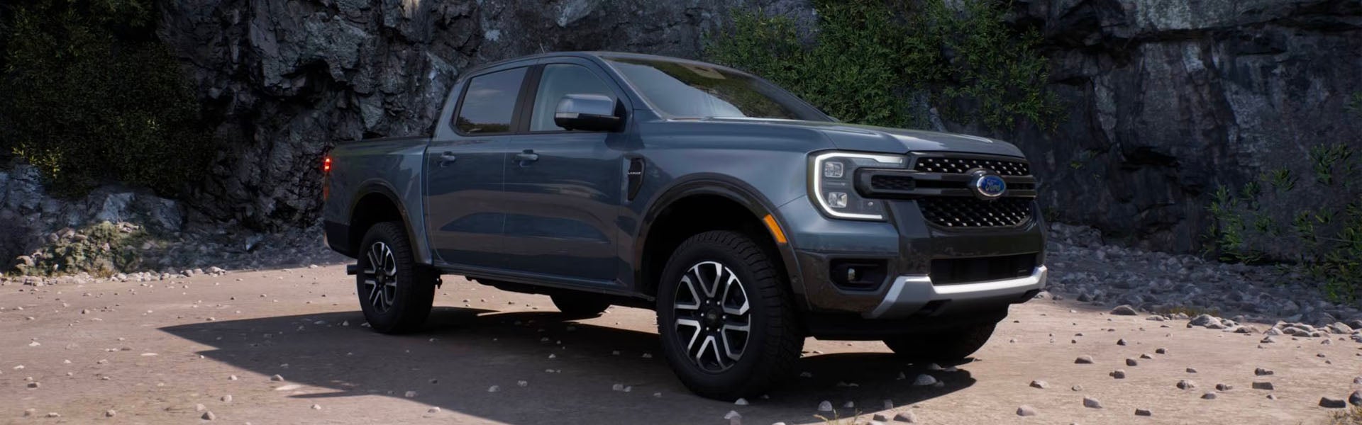 Dark blue Ford Ranger pickup truck parked on a gravel path with rocky cliffs and green foliage in the background.