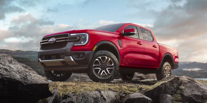 Red Ford pickup truck parked on rocky terrain with mountains and a cloudy sky in the background.