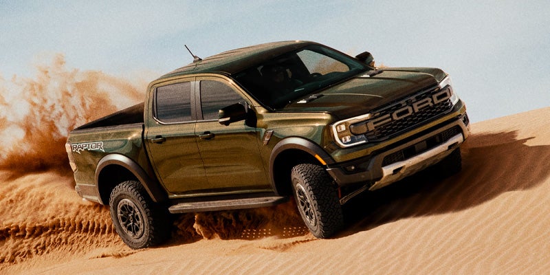 Dark green Ford Ranger Raptor pickup truck kicking up sand while driving in a desert.