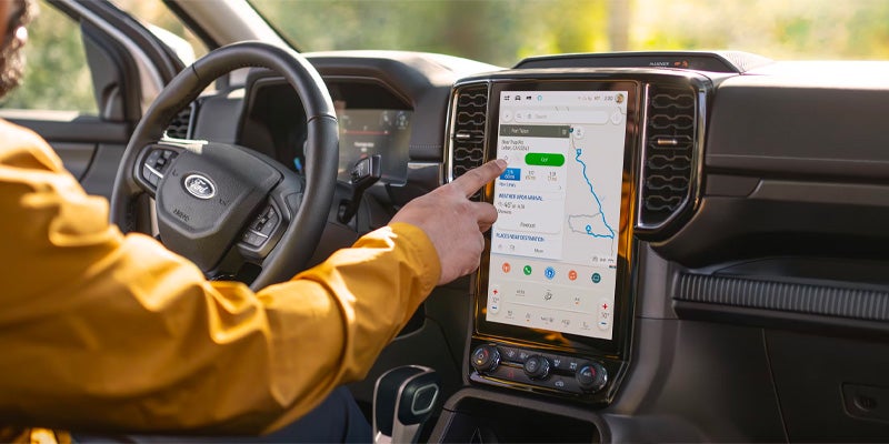 Close-up view of a Ford vehicle interior with a driver using the large touchscreen navigation system