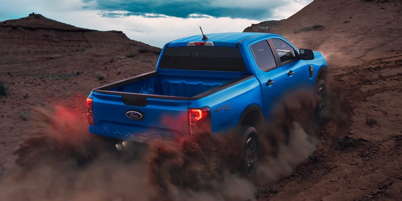 Blue Ford Ranger pickup truck driving off-road in a desert, kicking up a large cloud of dust from its rear wheels.