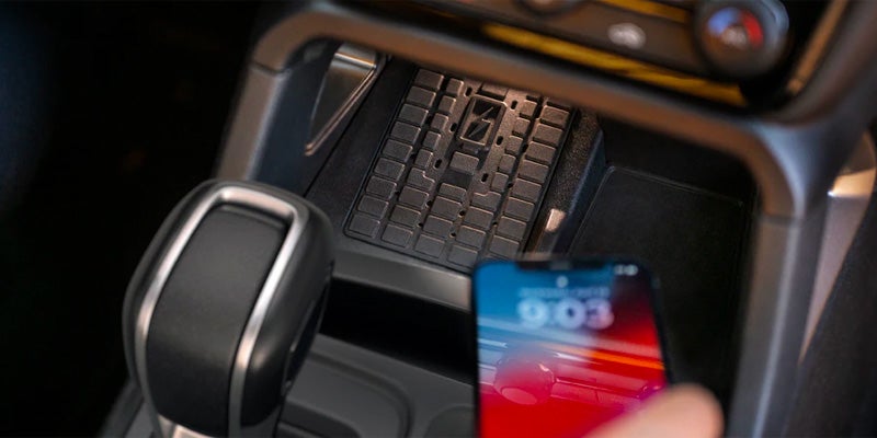 Hand placing a smartphone on a wireless charging pad in a car's center console next to the gear shift.