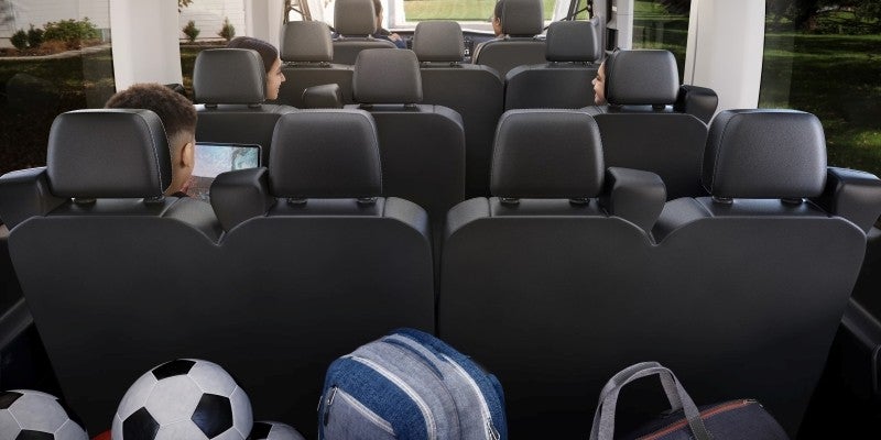 Spacious interior of a Ford Transit passenger van featuring multiple rows of black seats, with sports equipment