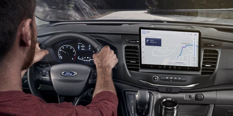 Driver’s view inside a Ford Transit van, showing hands on the steering wheel, a digital instrument cluster