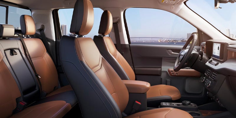 Car interior with two-tone brown and black seats, dashboard screen, and city skyline visible through the windows.