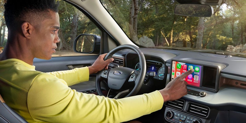Man in yellow shirt touches car's dashboard touchscreen while holding the steering wheel.