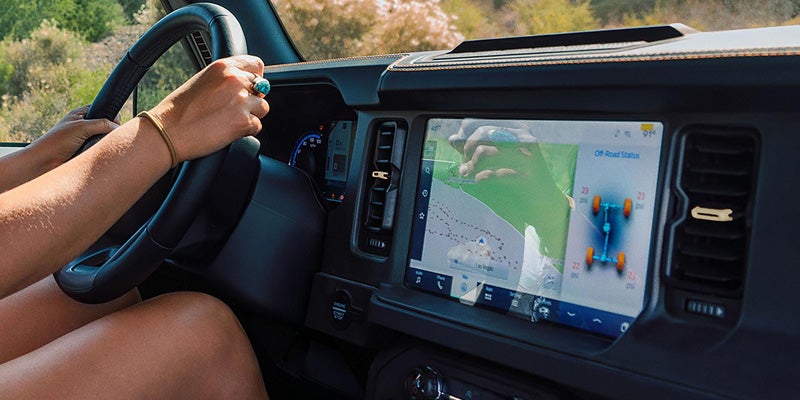 Hands on a steering wheel, with an infotainment screen showing a map and off-road status with tire pressures.
