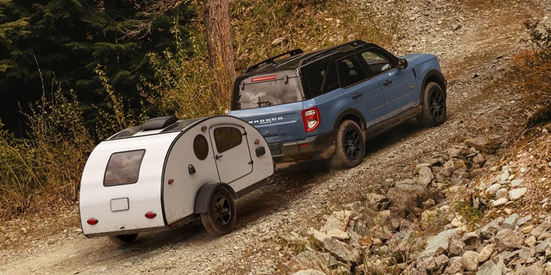 Blue SUV tows a white teardrop camper up a steep, rocky dirt road.