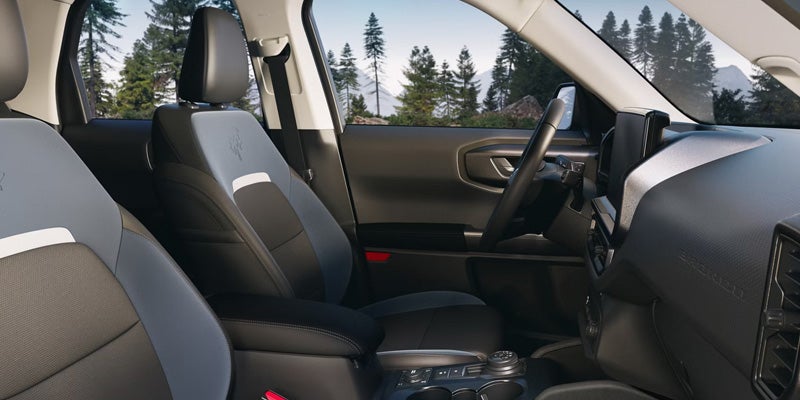 Car interior with gray and black two-tone seats, dashboard, and a view of trees and mountains outside.