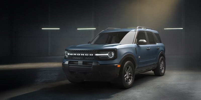 Blue Ford Bronco Sport SUV with headlights on, parked in a dark, industrial space.