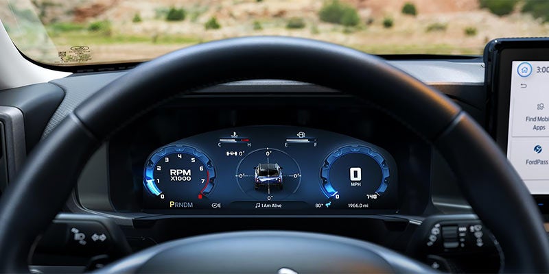 Car dashboard with a steering wheel and a digital instrument cluster displaying RPM and MPH.