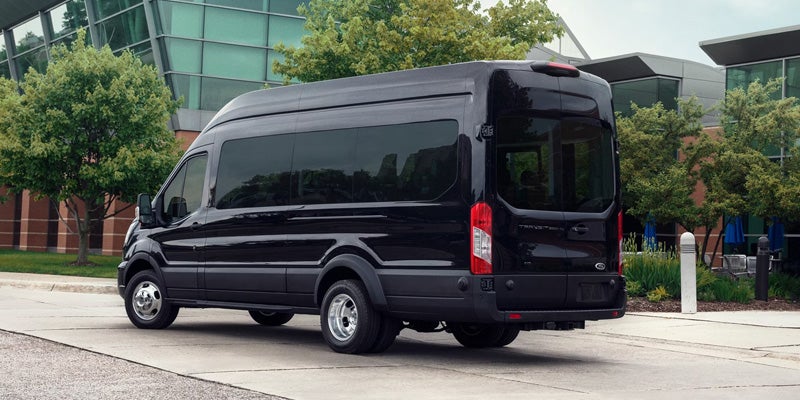 Black high-roof passenger van parked on pavement with modern buildings and trees in the background.