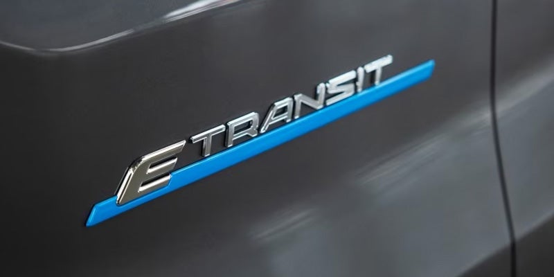 Silver 'E TRANSIT' emblem with a blue line underneath, on a dark grey vehicle surface.