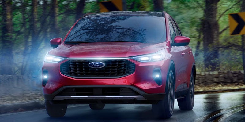 Red Ford SUV driving on a wet road at dusk, headlights and fog lights illuminated