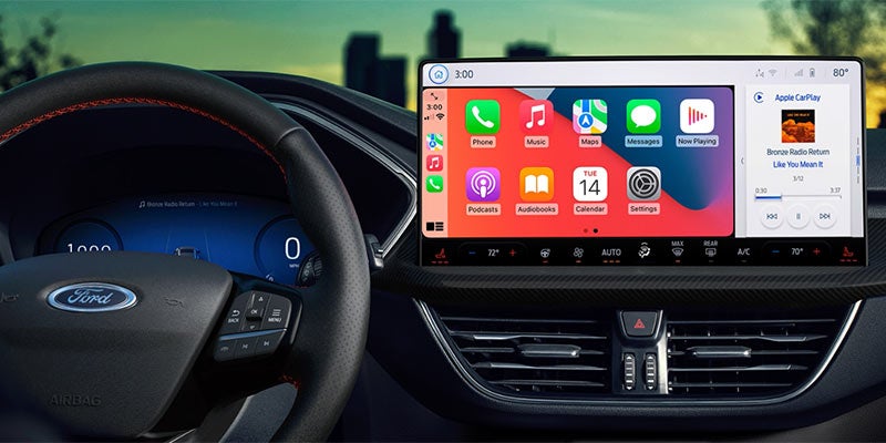 Car interior showing a steering wheel and a large infotainment screen displaying Apple CarPlay