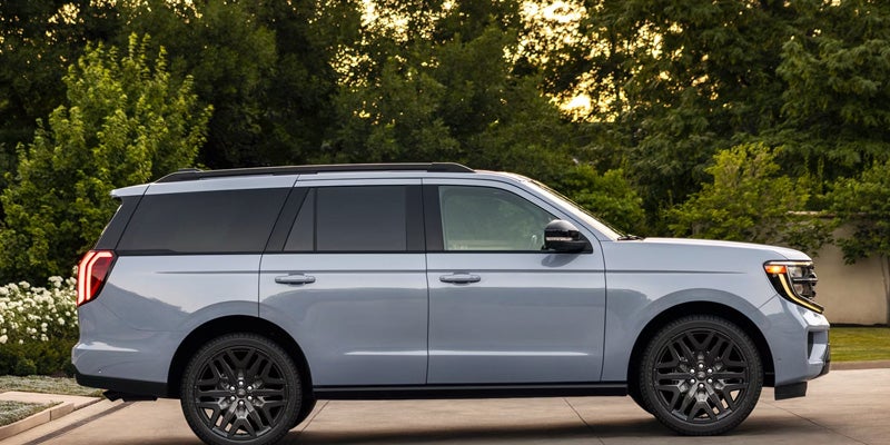 Light gray SUV parked outside, shown from the side with black wheels and green trees in the background
