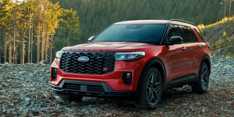 Red Ford Explorer SUV parked on rocky ground with a forest in the background