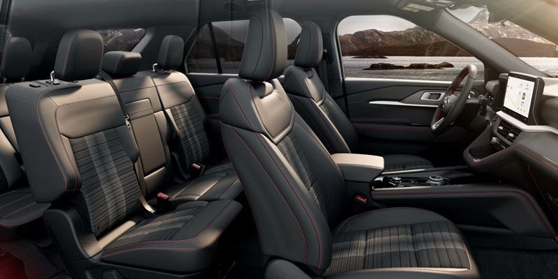 Modern car interior with dark seats, red stitching, and patterned fabric inserts, overlooking a lake and mountains.