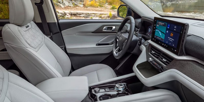 Light gray car interior with quilted driver's seat, black steering wheel, and large infotainment screen on the dashboard