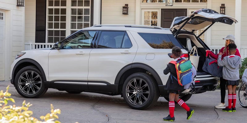 Family loading a white SUV with luggage in front of a house.