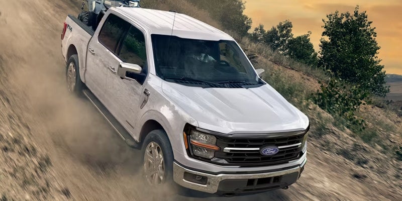 White Ford F-150 driving on a rugged dirt trail.