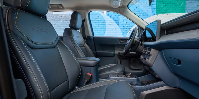 Interior of a car with dark blue seats, yellow stitching, Maverick branding, dashboard, steering wheel, and screen
