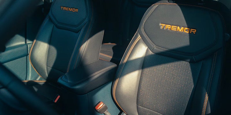 Black car seats with orange stitching and TREMOR logo embroidered on the headrests, bathed in sunlight