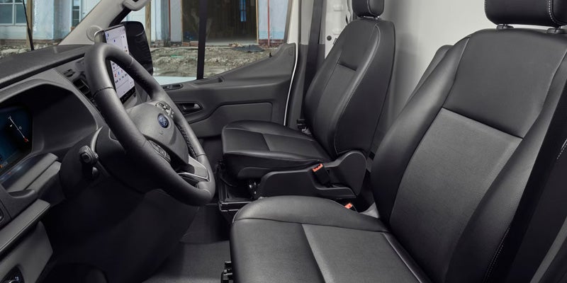 Black leather seats, steering wheel, and dashboard with a vertical screen inside a Ford Transit van.